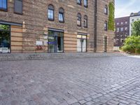 a motorcycle is driving down an empty street in a city corner, with cobblestone street