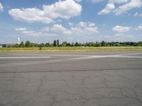 a street view looking across the empty runway at a forest and grassy area with clouds