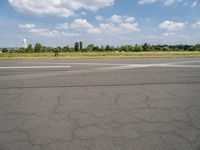 a street view looking across the empty runway at a forest and grassy area with clouds