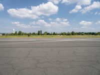 a street view looking across the empty runway at a forest and grassy area with clouds