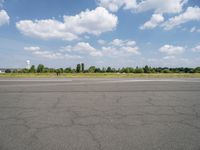 a street view looking across the empty runway at a forest and grassy area with clouds