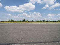 a street view looking across the empty runway at a forest and grassy area with clouds