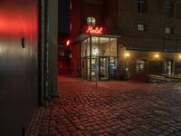 a brick street with a motel sign lit up at night outside a restaurant on a cobblestone pavement