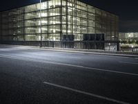 an empty street leading to a building lit up at night, with lights in the window