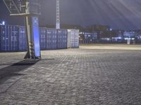 basketball net at night in a parking lot with lots of containers behind it and there is a ladder hanging