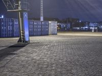 basketball net at night in a parking lot with lots of containers behind it and there is a ladder hanging