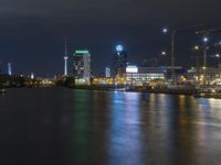 view over the city lights reflected on water of a river at night with building cranes