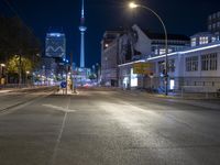 a city street is lined with trees, buildings and cars at night time near a light pole