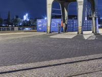 there is a train going over a bridge at night in the city square with blue containers