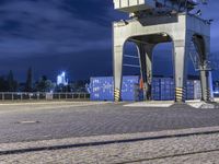 there is a train going over a bridge at night in the city square with blue containers