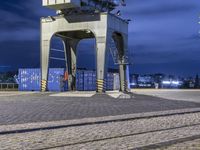 there is a train going over a bridge at night in the city square with blue containers