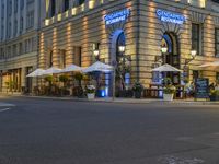 there are many tables and umbrellas in the evening near a building that is decorated in blue