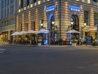 there are many tables and umbrellas in the evening near a building that is decorated in blue