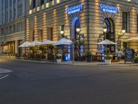 there are many tables and umbrellas in the evening near a building that is decorated in blue