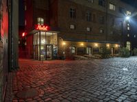 a stone sidewalk that has red neon signs on it in front of a building that has a restaurant next to it