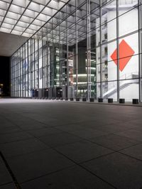a clock in a glass building in front of tall windows with lights from the ground