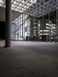 a clock in a glass building in front of tall windows with lights from the ground