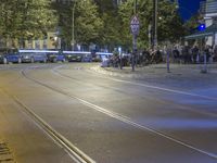 a train going down the street in a busy city at night with people and vehicles in front of the tracks