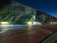 a mural is painted on the side of a building next to a road at night