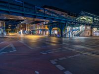 the empty street is filled with people walking and biking under an overpass at night