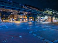 the empty street is filled with people walking and biking under an overpass at night