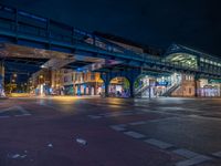 the empty street is filled with people walking and biking under an overpass at night