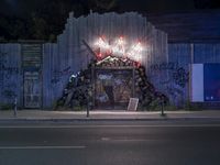 a view at night in the street of a fence and graffiti wall decorated with a door