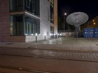 two satellite dishes suspended over a street next to a curb and building at night in the background