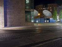 two satellite dishes suspended over a street next to a curb and building at night in the background