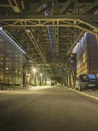 a black car parked underneath an elevated bridge at night on a city street in the city