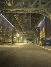 a black car parked underneath an elevated bridge at night on a city street in the city