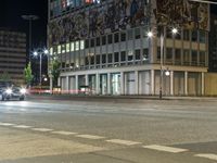 cars are traveling around a city street at night time with lights on the side of a building