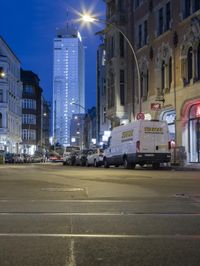 a large group of white vans in a city street at night with other cars and pedestrians