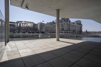 an empty walkway leading to an enormous building in a city with tall windows overlooking the lake