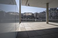 an empty walkway leading to an enormous building in a city with tall windows overlooking the lake