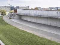 a concrete building sits on a grass field with some people on a bike trail and several buildings