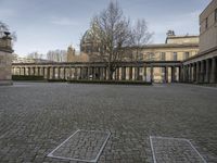 a picture of a courtyard with a few columns on the left and a small garden with benches in front