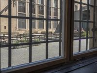 an outdoor patio with tables and benches, viewed through a window in a building with brick walls, has a bench outside