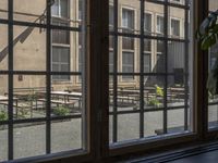 an outdoor patio with tables and benches, viewed through a window in a building with brick walls, has a bench outside