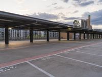 a parking structure in the evening at a bus station next to some buildings is empty and has many signs and numbers