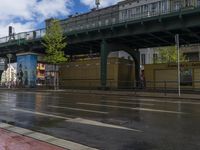 a street that is next to a bridge on a rainy day with an umbrella and two people in front