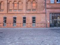 the building is made of red brick with doors and windows there is a man walking down a cobble stone sidewalk