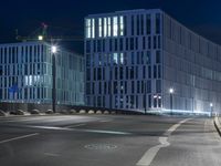 large building on the street with lights in front and other buildings nearby at night with no one moving