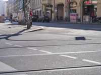 a street with no cars on it with people walking across the road and cars driving past