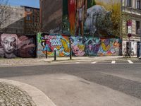 a wall with different colorful artwork on it in a city with buildings around and the street has a bike path going under it