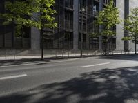 a road in front of an apartment building with lots of glass walls and trees on the side