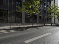 a road in front of an apartment building with lots of glass walls and trees on the side