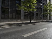 a road in front of an apartment building with lots of glass walls and trees on the side