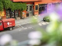 a red delivery truck is parked outside of a restaurant near the street with flowers growing out of the window