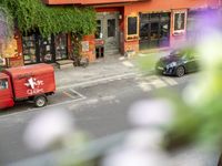 a red delivery truck is parked outside of a restaurant near the street with flowers growing out of the window